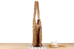 Detail of a brown hand-woven paper rope tote bag with fabric lining on a wooden desk