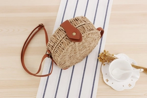 Top view of a round straw crossbody bag with leather strap on a rustic wooden table