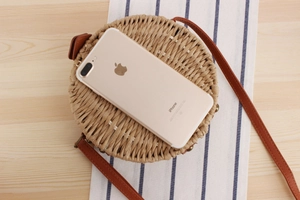 Flat lay of a round woven crossbody bag with brown leather strap on a wooden table