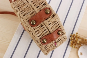 Close-up of woven straw round crossbody bag showing leather straps and brass rivet details