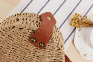 Close-up of woven straw texture and leather strap with bronze rivets on a round bag