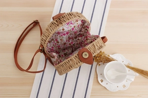 Detail of round straw crossbody bag showing floral lining and magnetic metal buckle