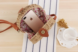 Close-up of circular straw bag with floral lining and leather strap on a table