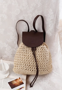 Detail of woven straw backpack with dark brown leather flap on a lace background