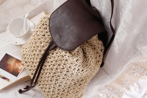 Detail of hand-woven straw backpack with brown leather straps on a white lace background