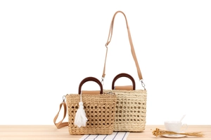Detail of woven straw handbag with wooden handle and fringe charm in two colors