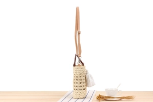 Close-up of woven straw bag with fringe tassel, leather strap and wooden handle