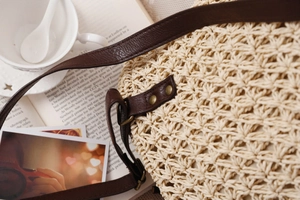 Detail of hand-woven beige paper rope bag with brown leather strap and brass rivets