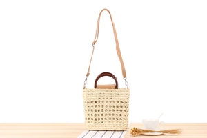 Detail view of handmade woven straw bag with round wooden handles and detachable shoulder strap