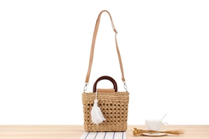 Detail of woven straw handbag with wooden handle and fringe tassel on wood table