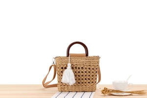 Close-up of straw woven handbag with wooden handle, white tassel and crossbody strap