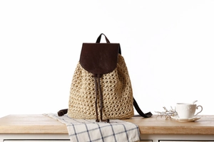 Close-up of woven straw texture and dark brown leather flap on a stylish beach backpack
