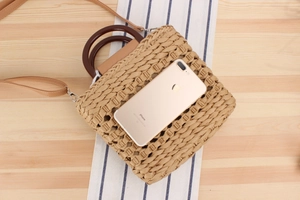 Detail of woven straw handbag with wooden ring handles and a mobile phone for size reference
