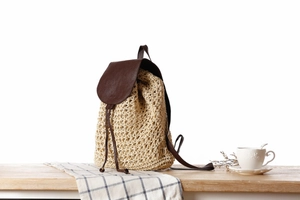 Detailed view of woven paper rope backpack with brown leather lid on a wooden table