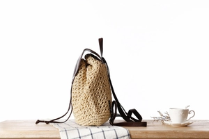 Detail of beige paper rope woven backpack with brown faux leather flap and drawstring