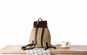 Detail of woven straw backpack with brown leather trim and metallic rivet accents