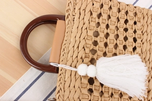 Detail of woven straw bag with dark round handles and decorative long white tassel