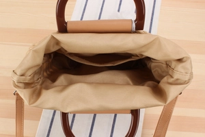 Top view of woven tote interior with brown round handles, fabric lining and shoulder strap