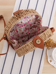Handmade round straw crossbody bag with floral lining and brown leather strap on wooden table