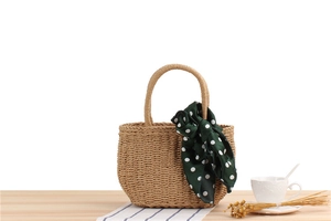 Detail of hand-woven straw tote bag with green polka dot silk scarf on a wooden table