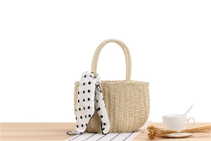 Close-up of handmade woven straw bag with polka dot scarf detail on a wooden table