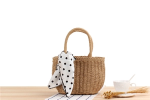Detail of hand-woven straw tote bag with elegant black polka dot scarf on wooden table