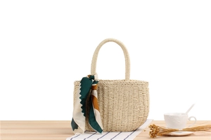 Detail of hand-woven beige straw bag featuring a stylish green and brown silk scarf handle