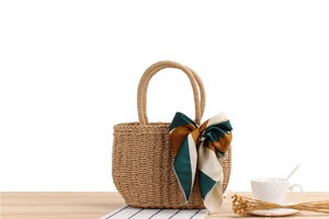 Detail of handmade beige straw beach bag with a colorful silk scarf on wooden surface