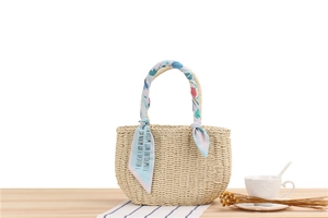 Detail of hand-woven straw beach bag featuring a colorful floral silk scarf on the handle