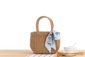 Detail of hand-woven straw tote bag with floral scarf handle on a white background