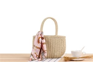 Detail of handmade woven straw bag with pink floral silk scarf on a wooden table