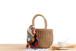 Handwoven straw bag with round base and decorative floral scarf on a resort-style setting