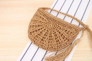 Detail of handmade woven straw crossbody bag with fringe tassels on blue striped fabric