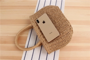 Detailed top view of handmade semi-circular woven straw bag with round handles on a desk