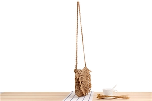 Detailed close-up of handmade straw shoulder bag with long fringes on wooden table