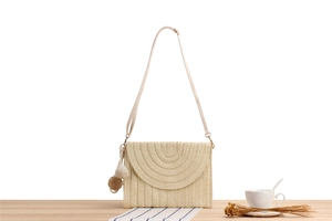 Gros plan sur le sac bandoulière beige fait main en papier tressé avec pompons