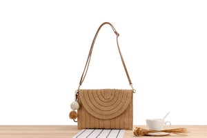 Vue détaillée du sac bandoulière en paille tressée avec pompons sur une table en bois