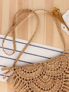 Handmade woven crossbody bag with fringe details on a natural wood background