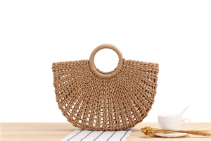 Detail of hollow woven paper straw handbag with round handles on a wooden table