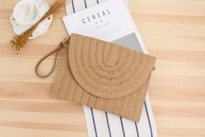 Détail de pochette en paille tressée avec rabat demi-lune sur table en bois naturel