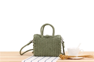 Detail of green woven crossbody bag with round handle on a wooden table with stripes