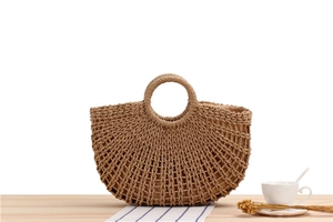 Detail of hollow-out woven straw handbag with a round handle on a wooden table