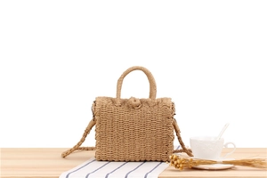 Detail of hand-woven straw crossbody bag on a wooden table with casual decor