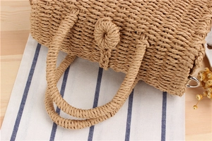 Detail of woven straw handbag featuring a spherical clasp and rustic woven handle
