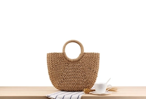 Detail of hand-woven straw bag with round handle and natural texture on wooden desk