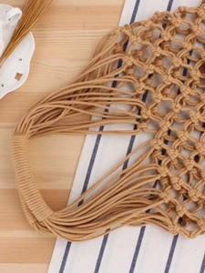 Handmade woven cotton rope beach bag in khaki with diamond hollow mesh on wooden background