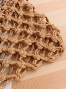 Handmade woven hollow mesh beach tote bag in natural khaki cotton rope with wooden backdrop