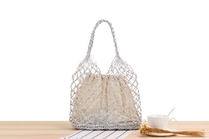 Close-up of silver metallic woven tote bag with beige drawstring lining on a wooden desk