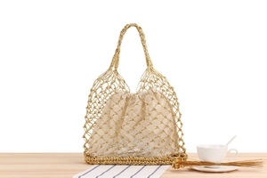Detail of woven gold handbag with beige drawstring pouch on a wooden table setup