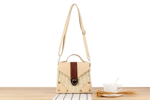 Detail of woven straw handbag featuring brown leather flap and gold metal buckle closure